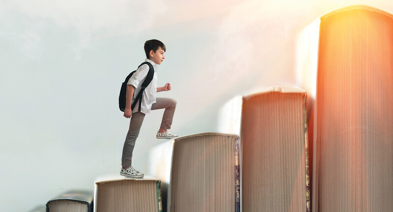 A young male student with a backpack walks up a row of book spines arranged like a staircase