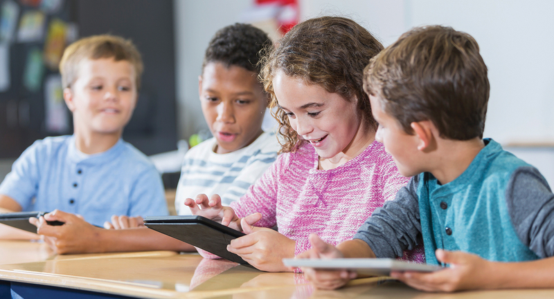 A group of young students looks happily at an iPad as they click the screen